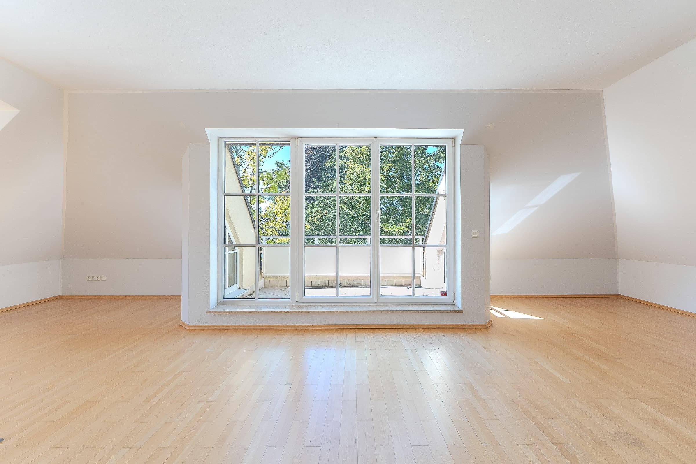 Lichtdurchflutetes Dachgeschoss eines Hauses mit Blick auf Bäume und die umliegende Dachlandschaft