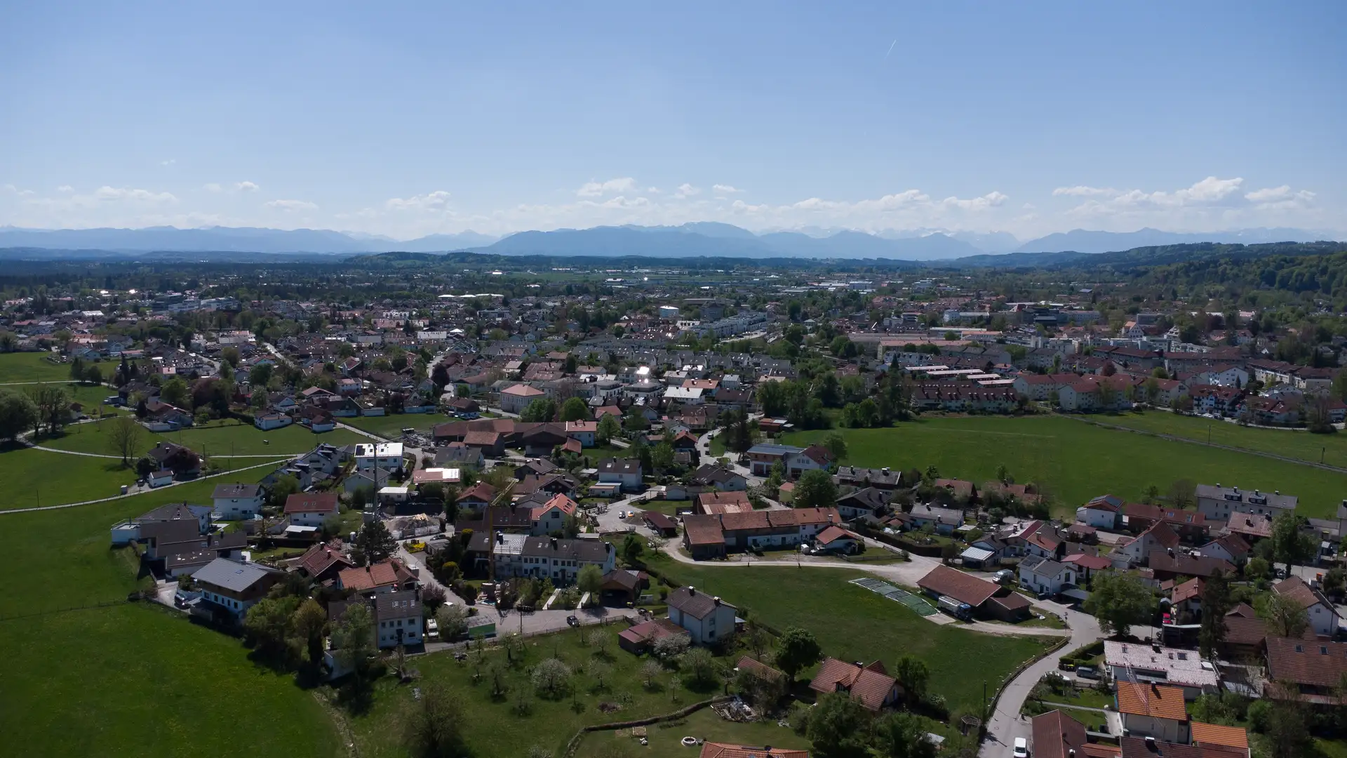 Panorama über Wolfratshausen mit Wohnlagen, Wiesen und der Alpenkette am Horizont