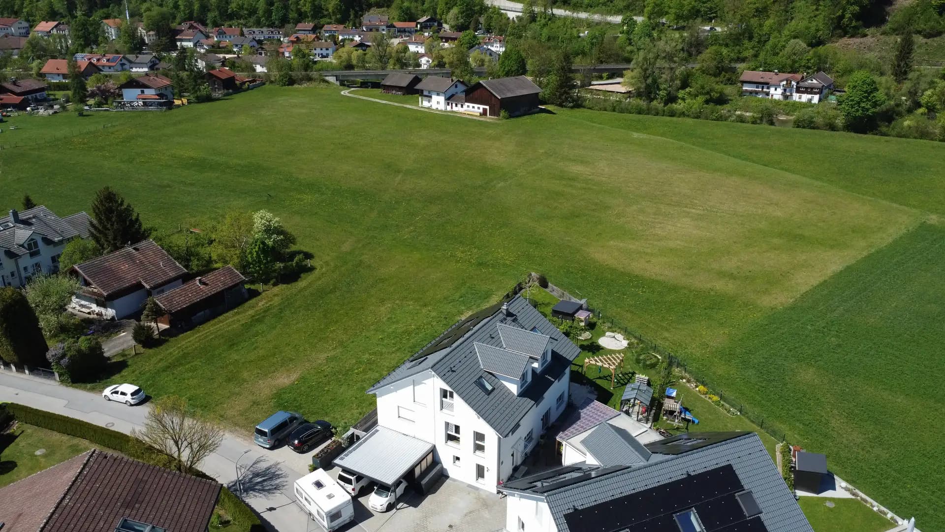 Wohnhaus am Wiesenrand von Wolfratshausen, dahinter Bebauung und bewaldeter Talhang