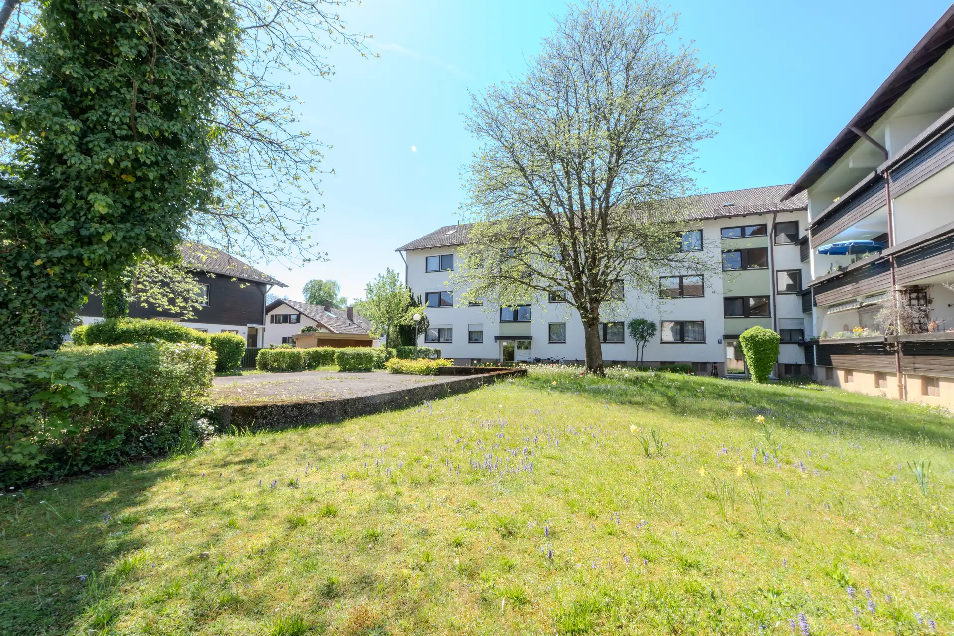 Gartenseite einer gewachsenen Wohnanlage in Wolfratshausen mit blühender Wiese und altem Baumbestand